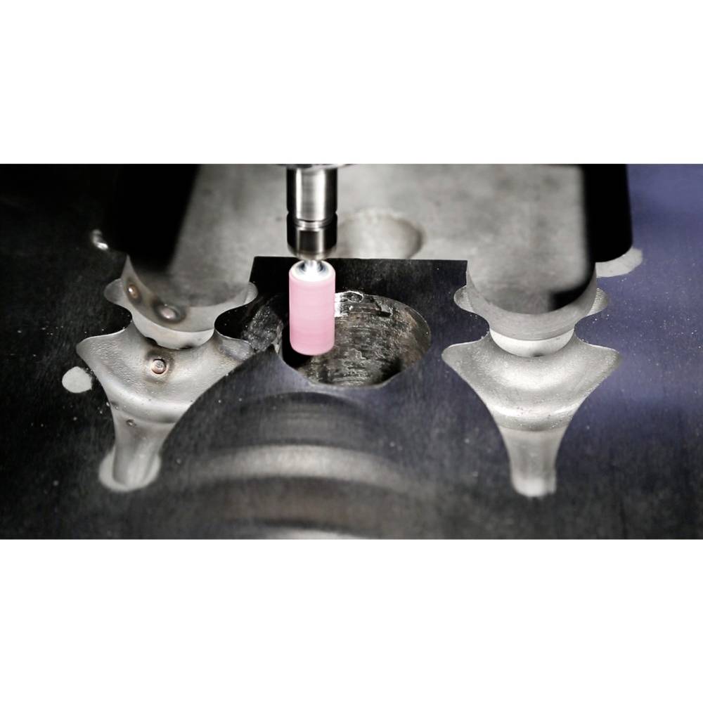Eine CNC-Maschine bearbeitet ein Metallstück mit hoher Präzision. Der Bohrer bearbeitet eine pinke Komponente auf dunkler Oberfläche.