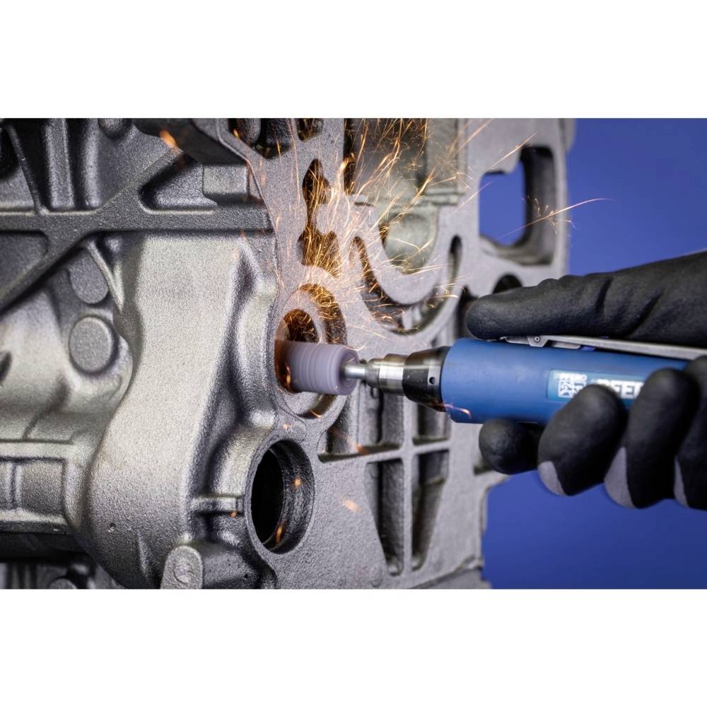 Eine Person schleift mit einem blauen Werkzeug Metall von einem grauen Motorblock ab, während Funken sprühen.