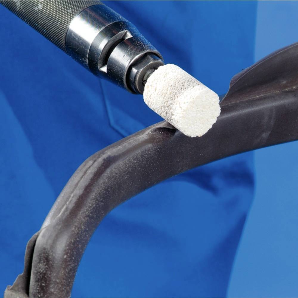 Nahaufnahme eines Bohrers, der Metall bearbeitet. Eine weiße Polierscheibe ist am Bohrkopf angebracht. Blauer Hintergrund.