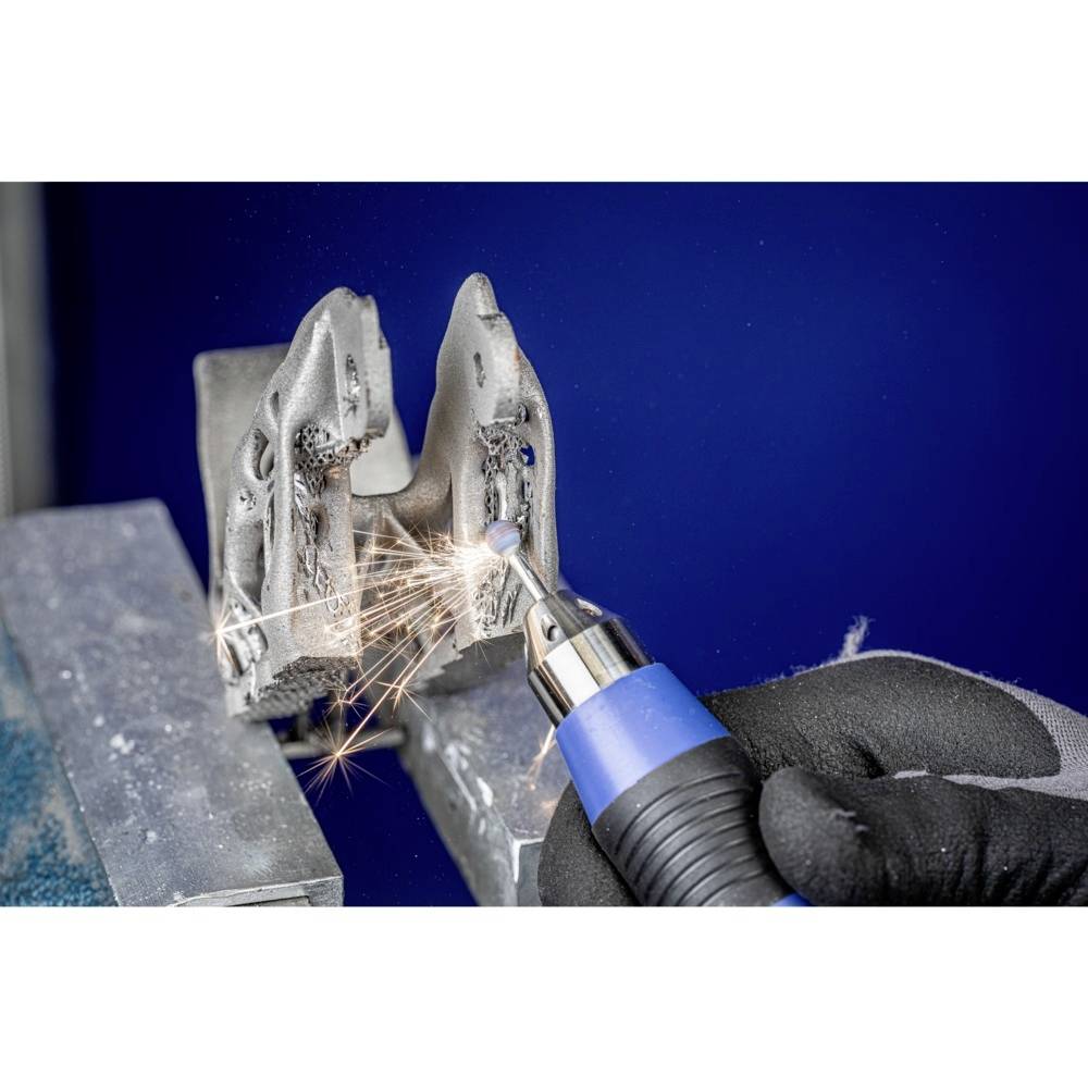 Eine Nahaufnahme zeigt eine Person in Handschuhen, die mit einem Werkzeug an einem metallischen Objekt arbeitet. Funken fliegen vom Kontaktpunkt.