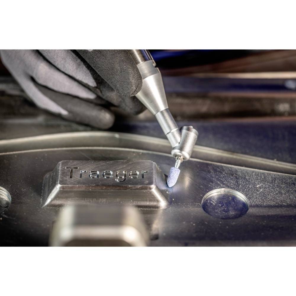 Eine Person bearbeitet eine Metalloberfläche mit einer Gravurwerkzeugspitze, auf der das Wort 'Traeger' eingraviert ist.