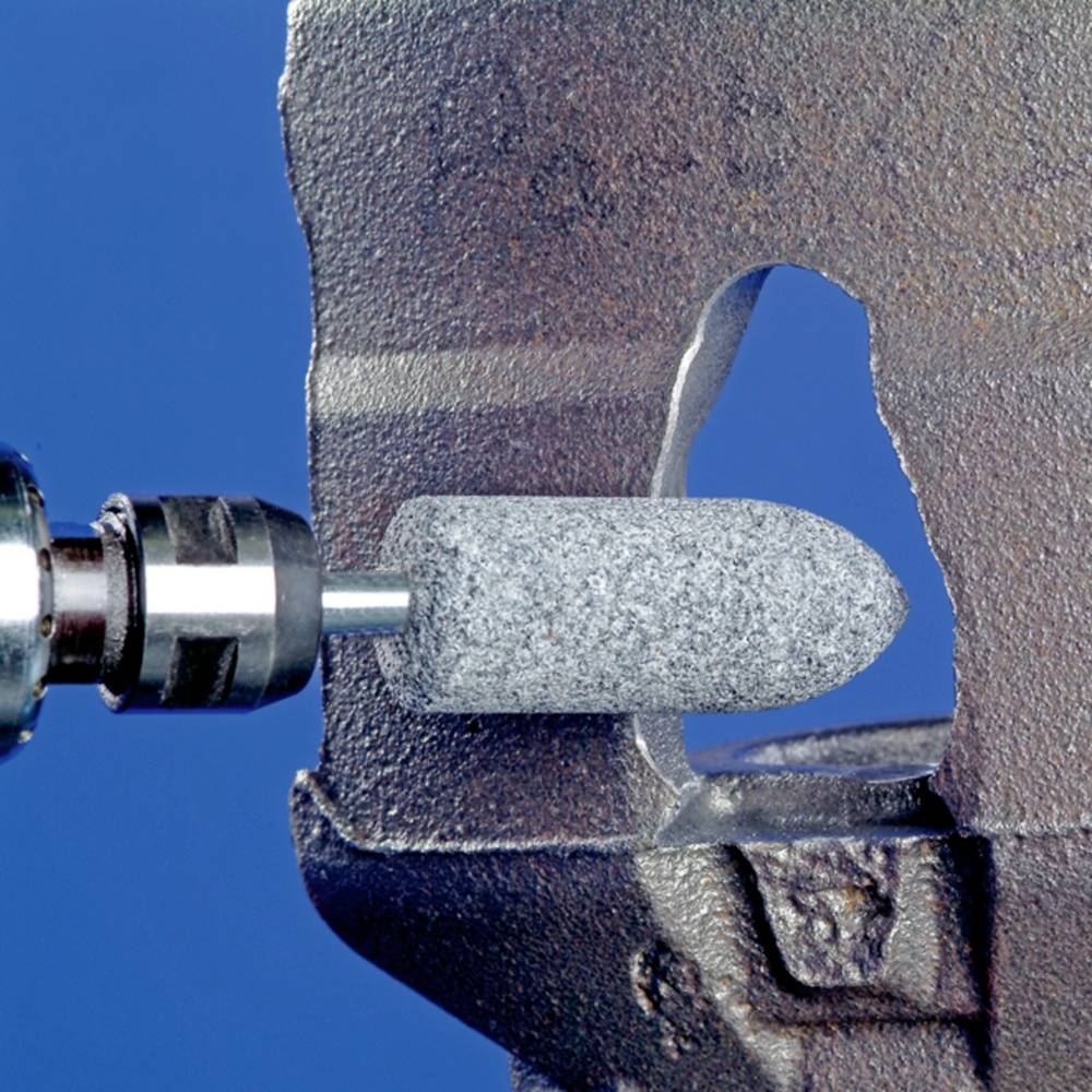 Ein metallisches Werkstück wird mit einem rotierenden Schleifaufsatz bearbeitet. Der Hintergrund ist blau.