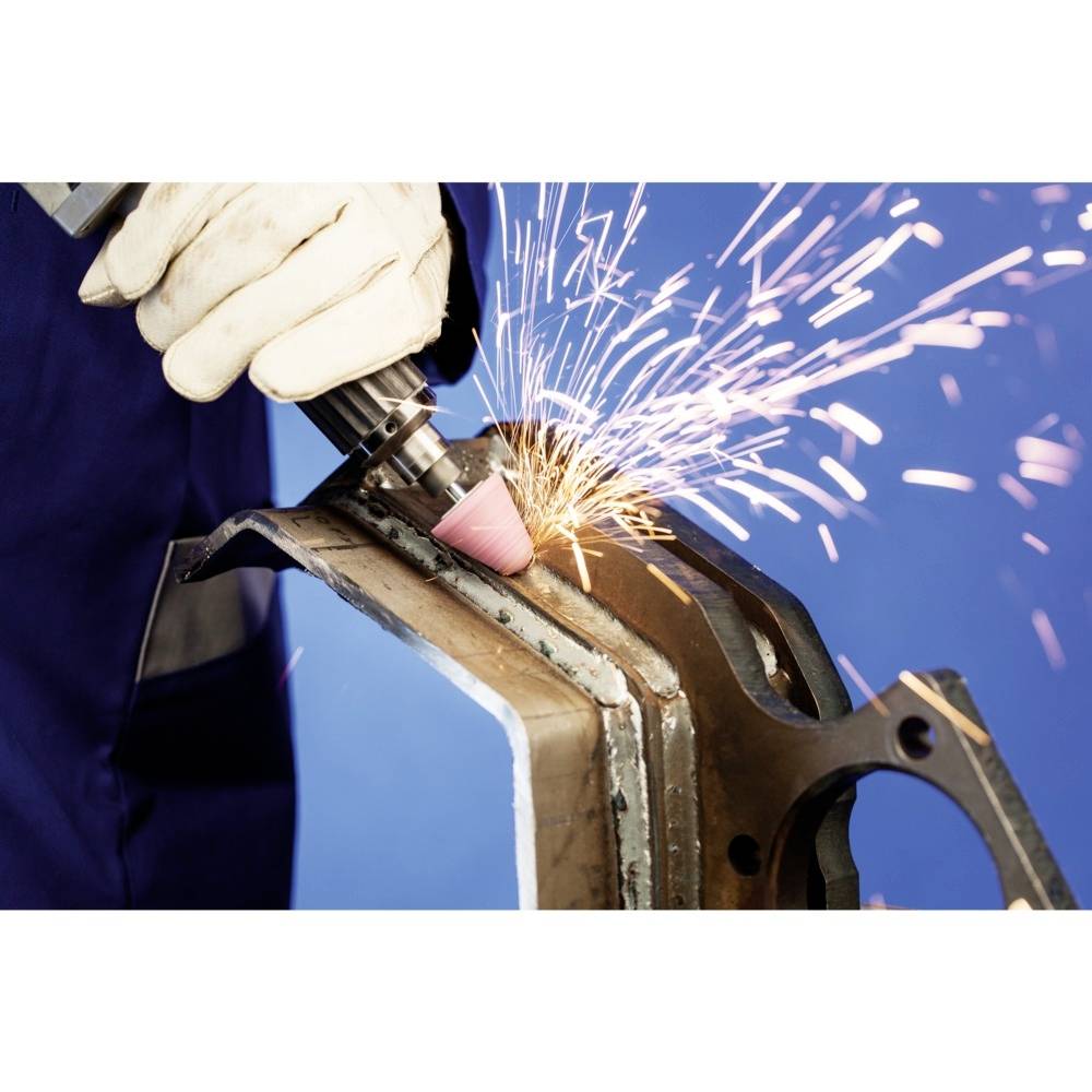 Arbeiter schleift eine Metallkante mit einem Winkelschleifer, Funken fliegen. Trägt Handschuhe und Schutzkleidung, blauer Hintergrund.