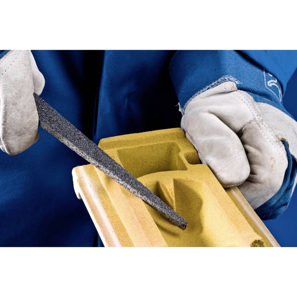 Eine Person feilt mit einer Metallfeile ein gelbes Schaumstoffstück. Die Hände sind in Handschuhen, der Person ist ein blauer Schutzanzug zu sehen.