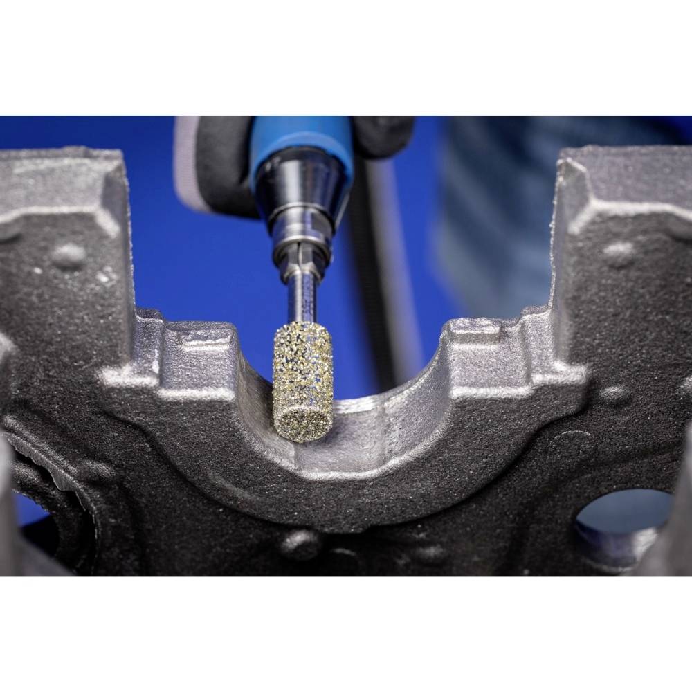 Eine Detailaufnahme zeigt eine Schleifmaschine, die eine Metallkante bearbeitet. Das Werkzeug hat einen zylindrischen Schleifkopf.