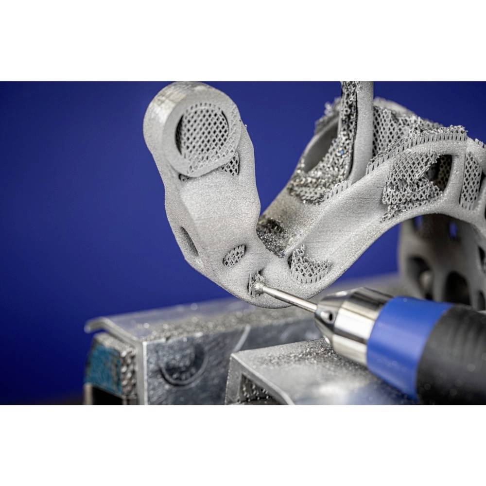 „Nahaufnahme eines 3D-gedruckten Metallteils, bearbeitet mit einem Werkzeug. Das Teil zeigt komplexe Gitterstrukturen.“
