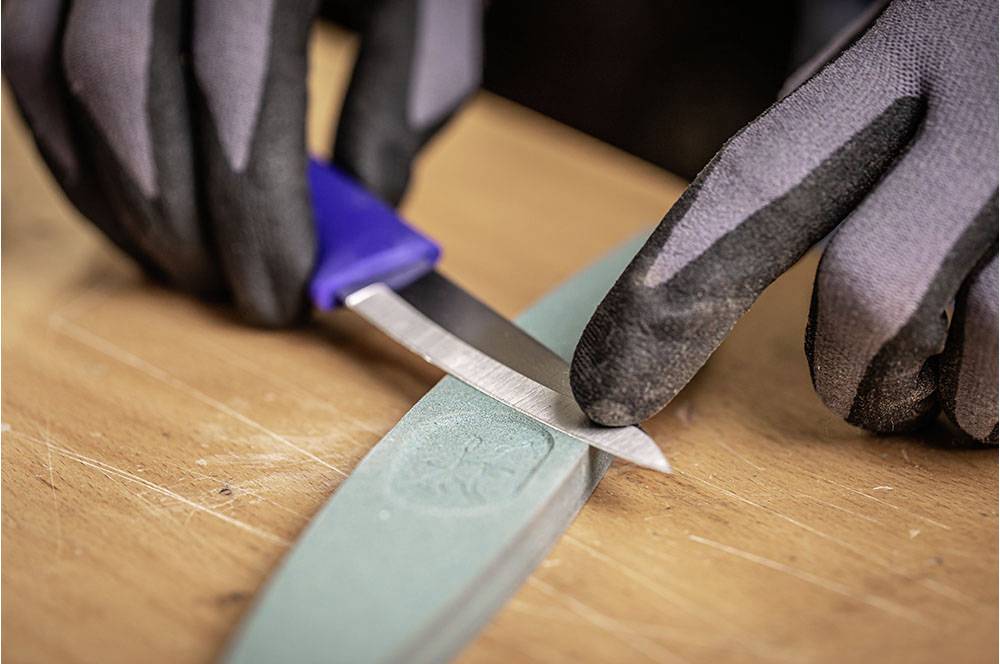 Eine Person schärft ein Messer auf einem Schleifstein. Sie trägt schwarze Handschuhe.