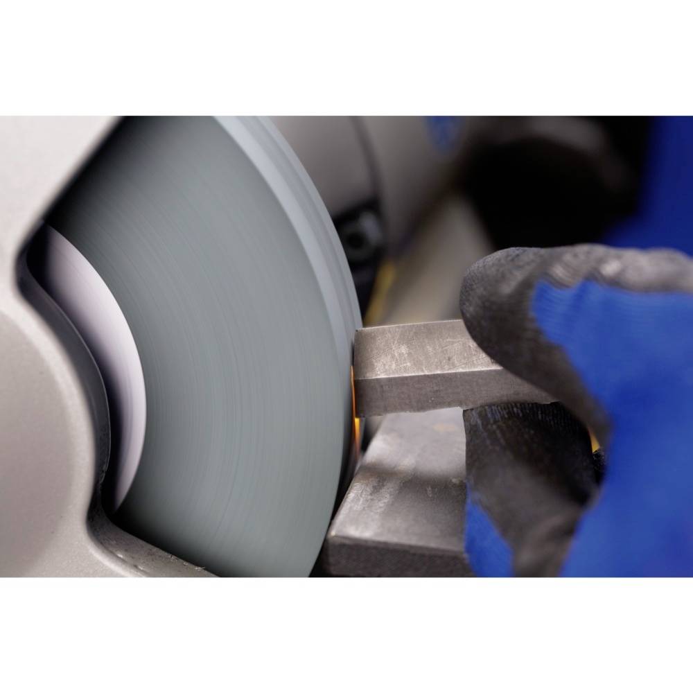 Eine Metallplatte wird von einer rotierenden Schleifscheibe bearbeitet. Ein Arbeiter trägt einen blauen Handschuh zur Sicherheit.