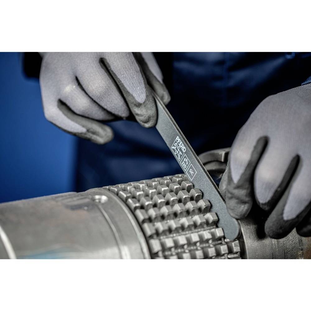 Person mit Handschuhen schleift eine Metallschnecke mit einer Feile, erkennbar an der Beschriftung und Symbolen auf der Feile.