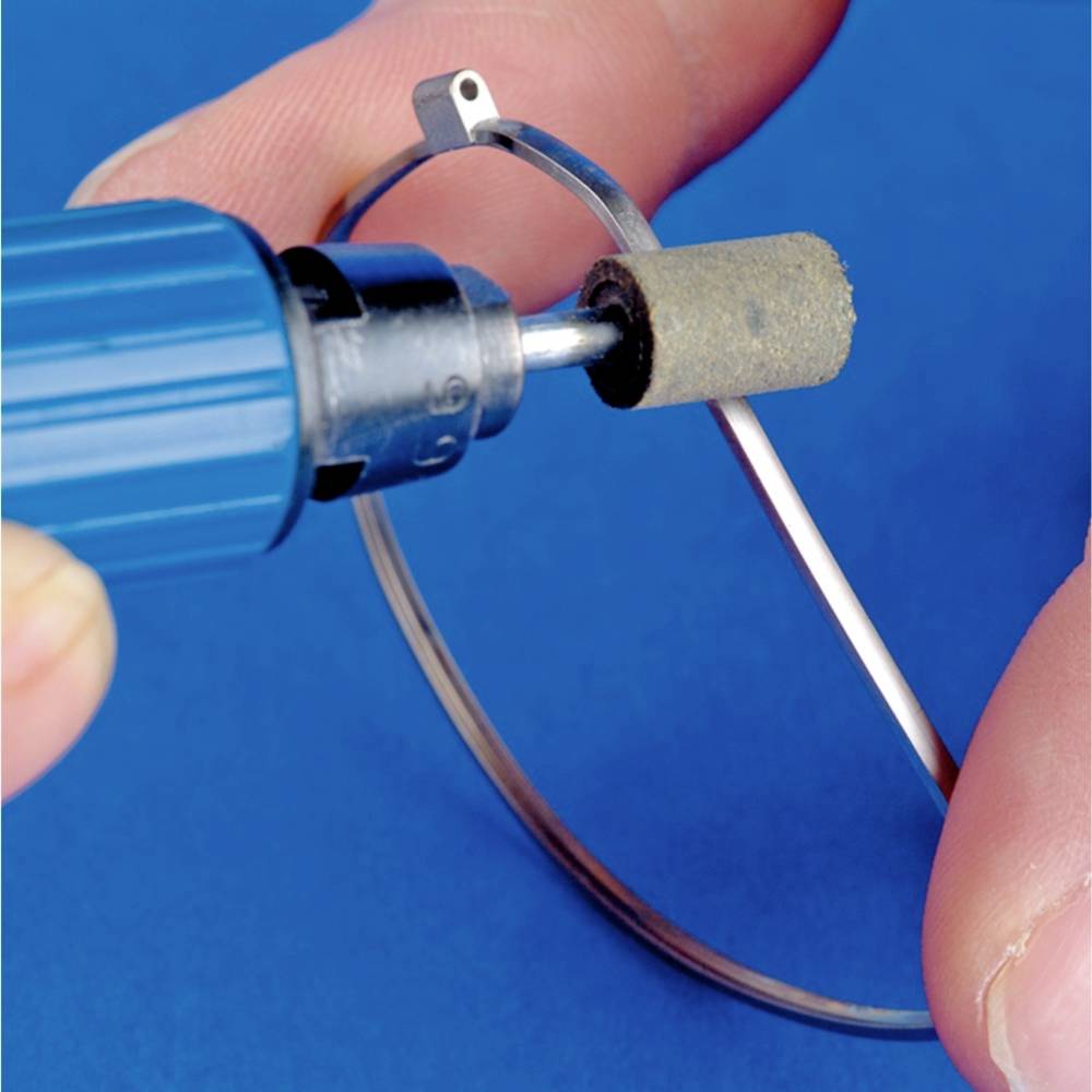 Nahaufnahme einer Hand, die einen rotierenden Schleifaufsatz verwendet, um einen Metallring zu bearbeiten, vor blauem Hintergrund.