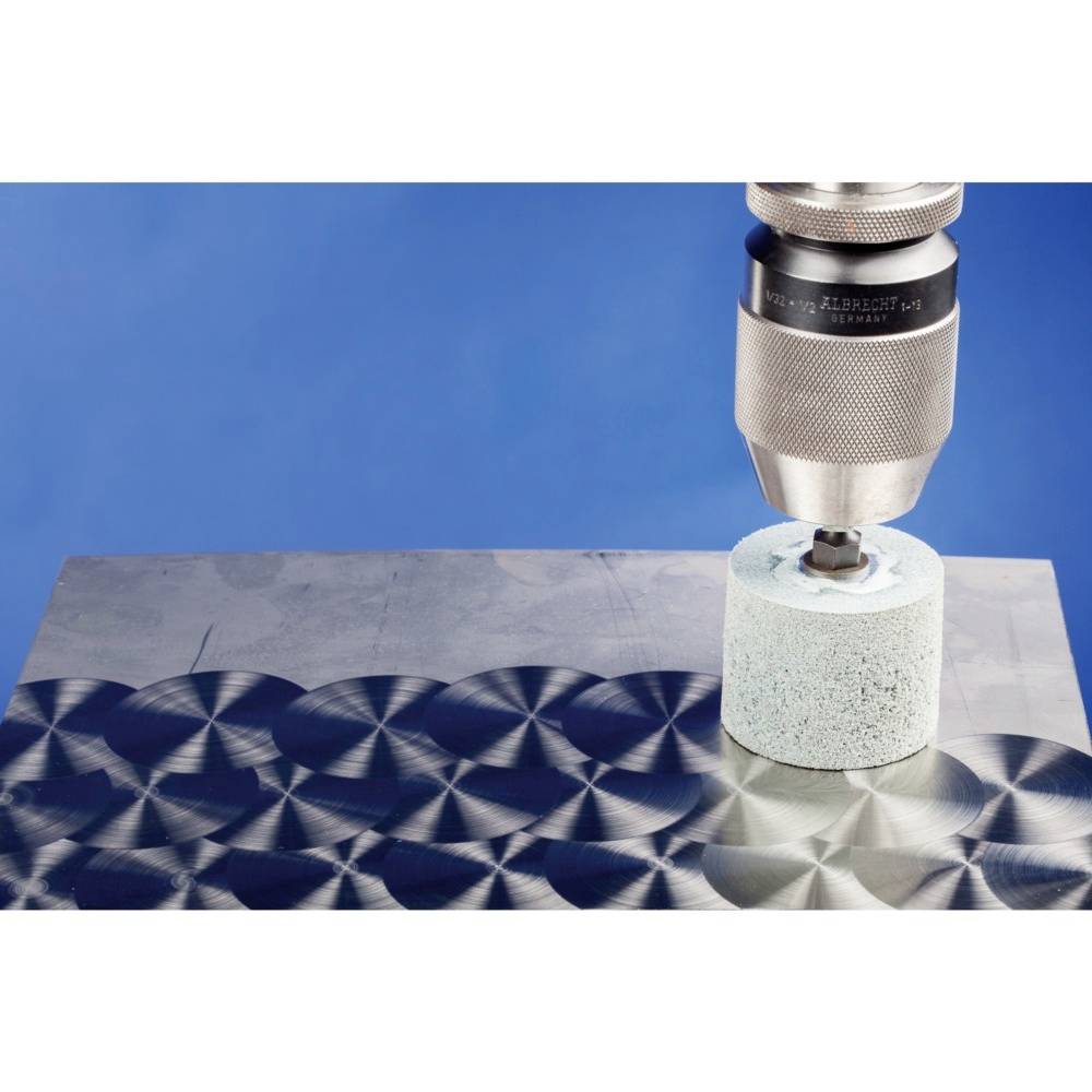 Nahaufnahme eines Bohrers, der ein poliertes metallisches Muster auf einer Stahlplatte erzeugt. Der Hintergrund ist blau.