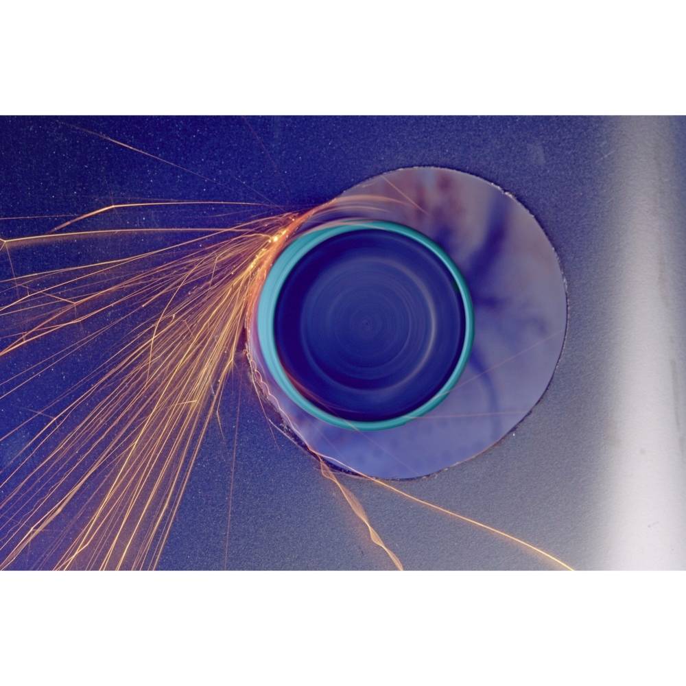 Funken sprühen von einer Kreissäge, die durch ein Metallblech schneidet. Ein blauer Hintergrund hebt die leuchtenden Funken hervor.