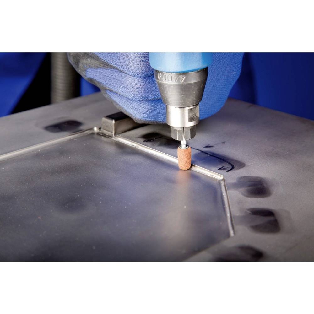 Eine Person trägt blaue Handschuhe und poliert eine Metallplatte mit einem rotierenden Werkzeug, um glatte Kanten zu erzeugen.