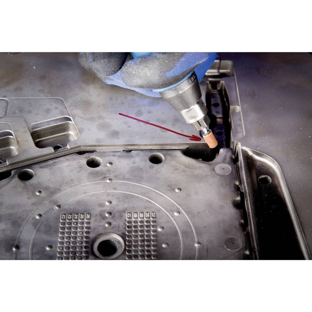 Nahaufnahme eines blauen Handschuhs, der eine Handwerkzeugspitze hält, um das Innere einer mechanischen Metallstruktur zu bearbeiten.