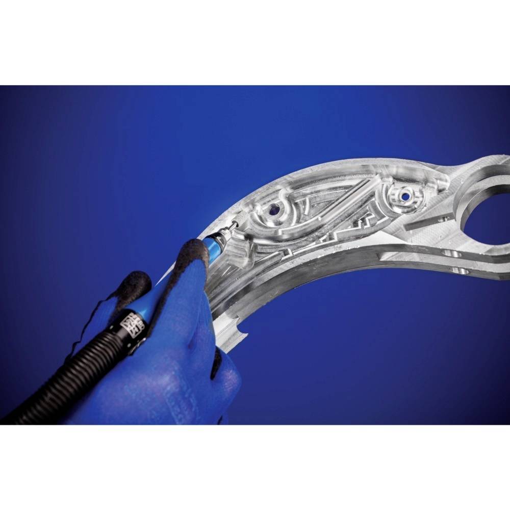 Eine Hand in einem blauen Handschuh hält ein Werkzeug und bearbeitet eine metallische Autoteil auf blauem Hintergrund.
