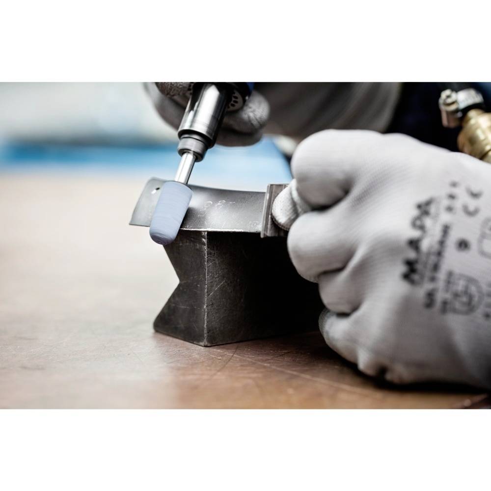 Eine Person bearbeitet ein Metallstück auf einem Amboss mit einer Schleifmaschine. Die Umgebung ist eine Werkstatt.