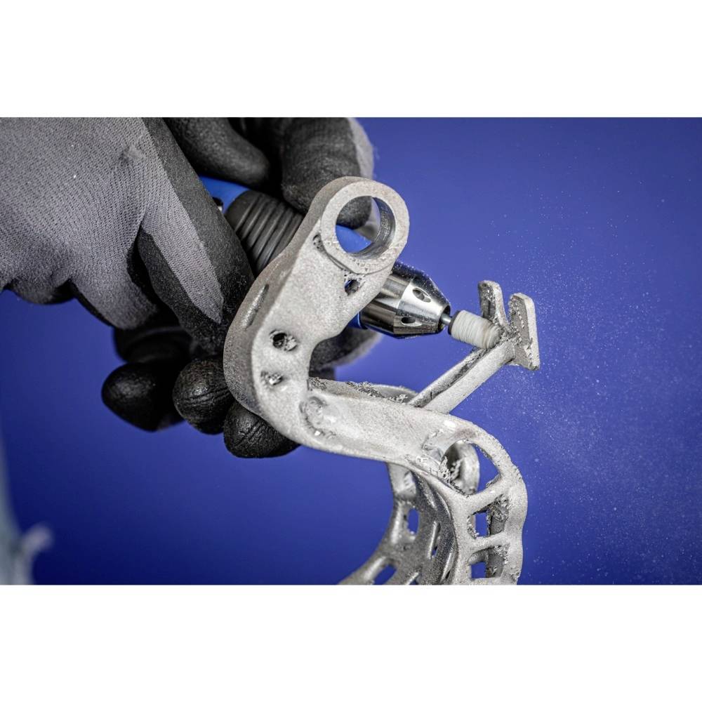 Eine behandschuhte Hand hält ein Metallteil, das mit einem rotierenden Werkzeug gegen einen blauen Hintergrund bearbeitet wird.