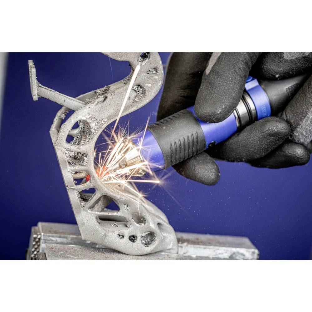 Eine Person trägt Handschuhe und schleift ein Metallobjekt mit einem Werkzeug, während Funken sprühen. Es handelt sich um eine präzise Arbeit.