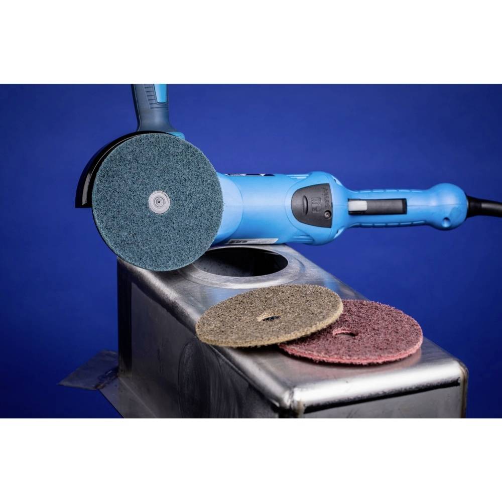 Ein Elektrowerkzeug mit rotierender Schleifscheibe bearbeitet eine Metalloberfläche. Zwei zusätzliche Schleifscheiben liegen daneben.