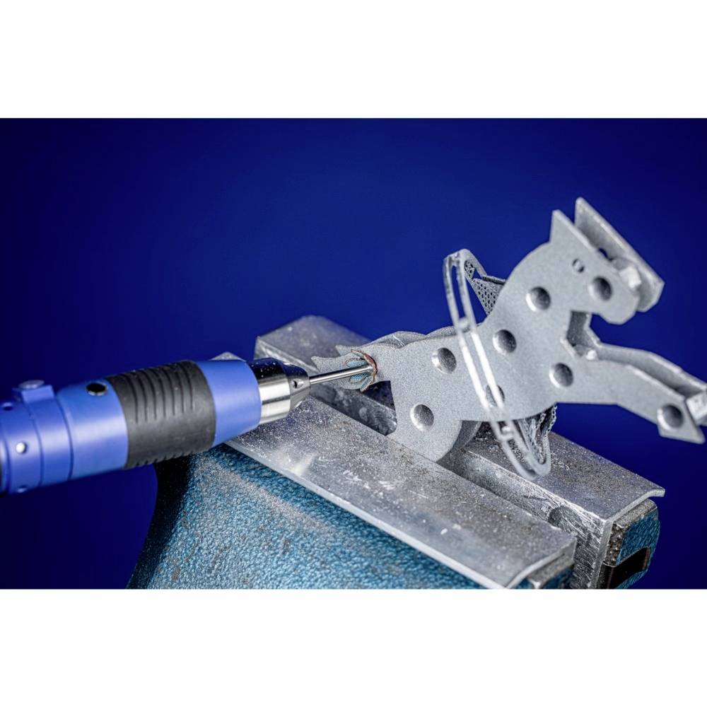 Eine blaue, elektrische Fräsmaschine bearbeitet ein graues Metallstück in Form eines Pferdes in einem Schraubstock.