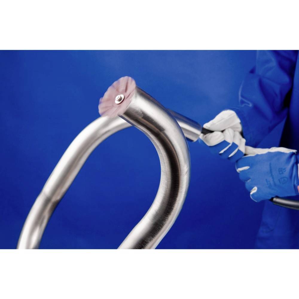 Eine Person mit blauen Handschuhen bearbeitet ein gebogenes Metallrohr mit einem Schleifgerät vor blauem Hintergrund.