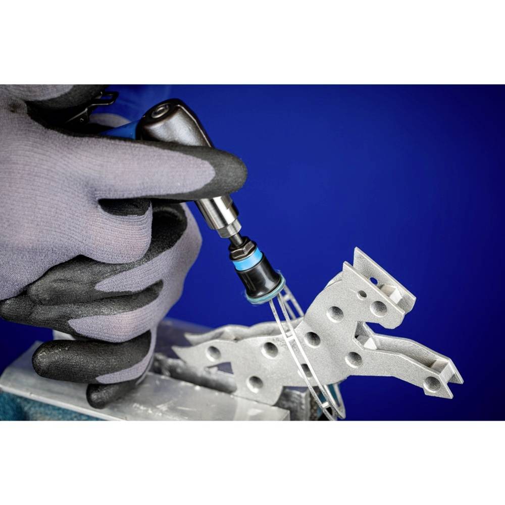 Ein Paar behandschuhte Hände hält ein kleines metallisches Werkstück in Form eines Pferdes und bearbeitet es mit einem rotierenden Werkzeug.