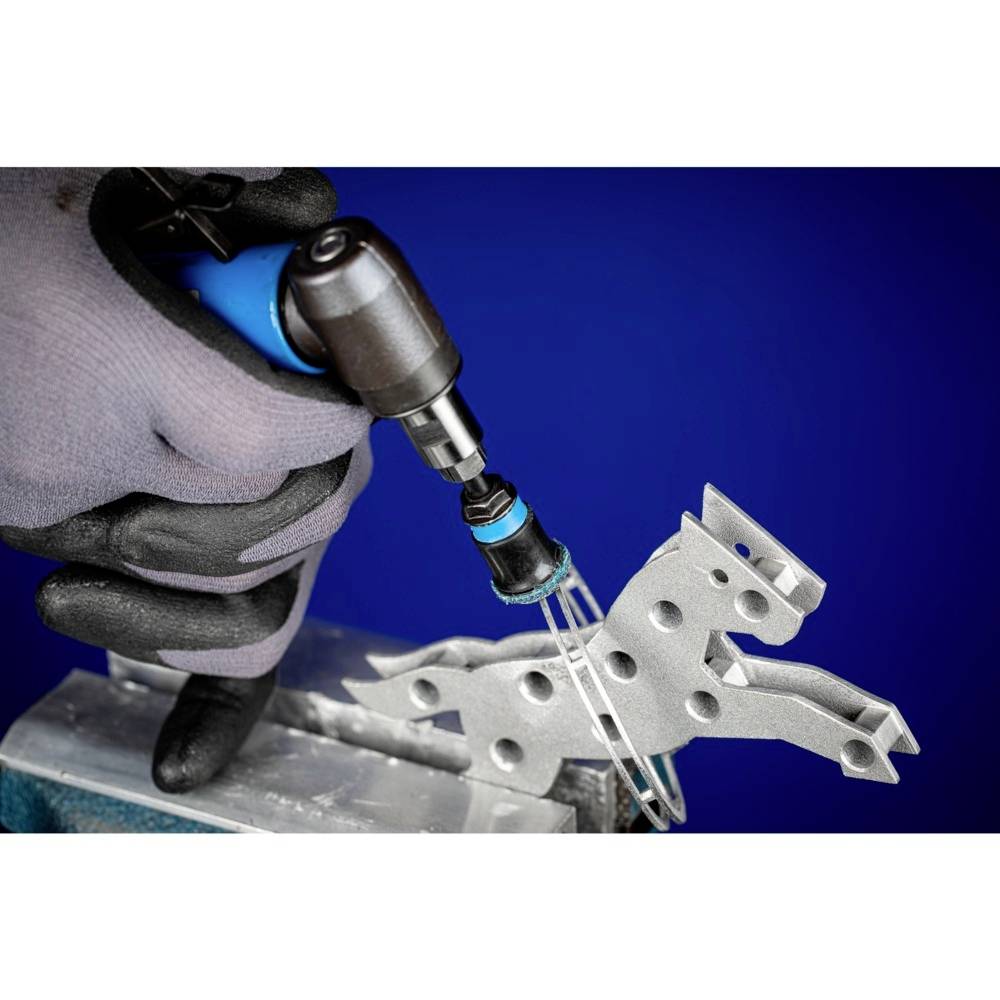 Eine Person mit Handschuh hält einen Metallbohrer, der ein Metallstück in Form eines Pferdes bearbeitet. Hintergrund ist blau.