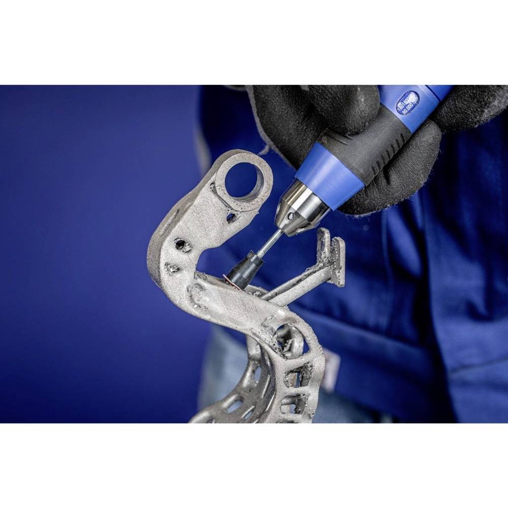 Eine Person mit Handschuhen bearbeitet ein Metallteil mit einem blauen, elektrischen Werkzeug vor einem blauen Hintergrund.