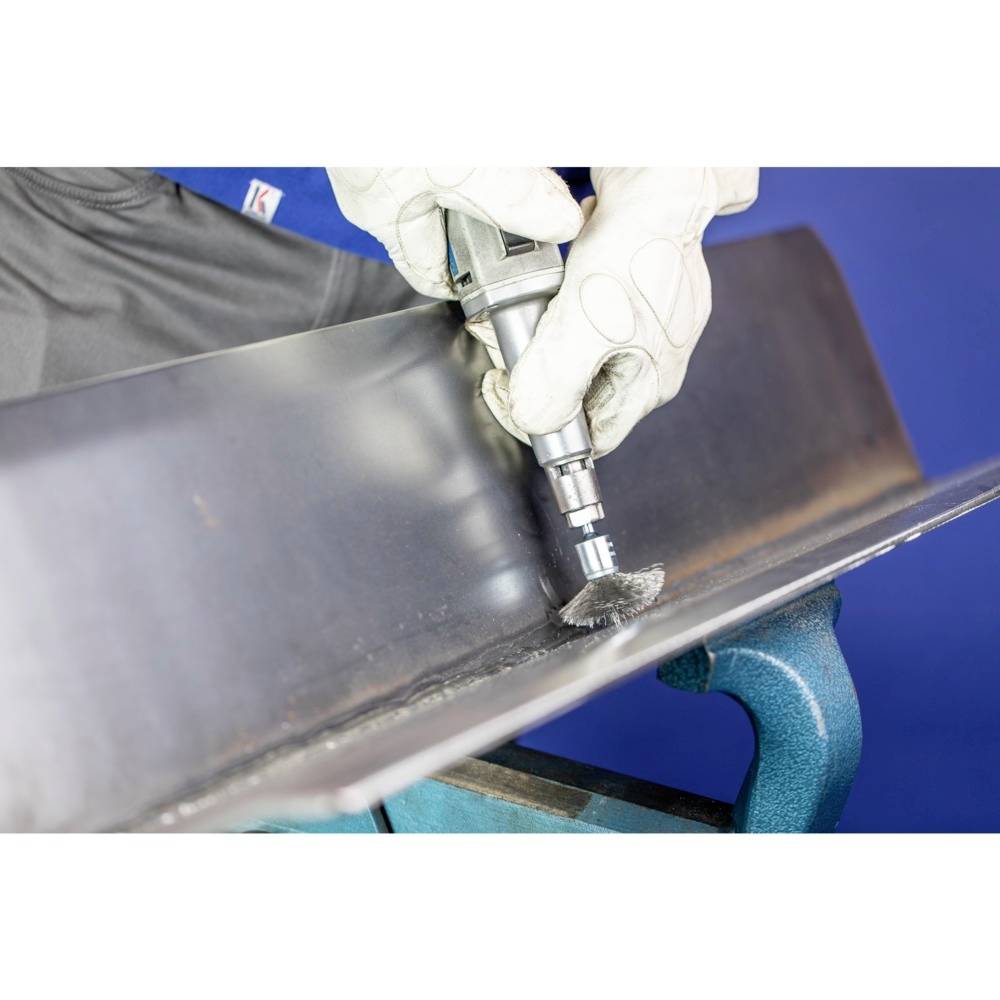 Person trägt Handschuhe und schleift eine Metallkante mit einem Elektrowerkzeug. Arbeitsumgebung and Werkzeug im Vordergrund.