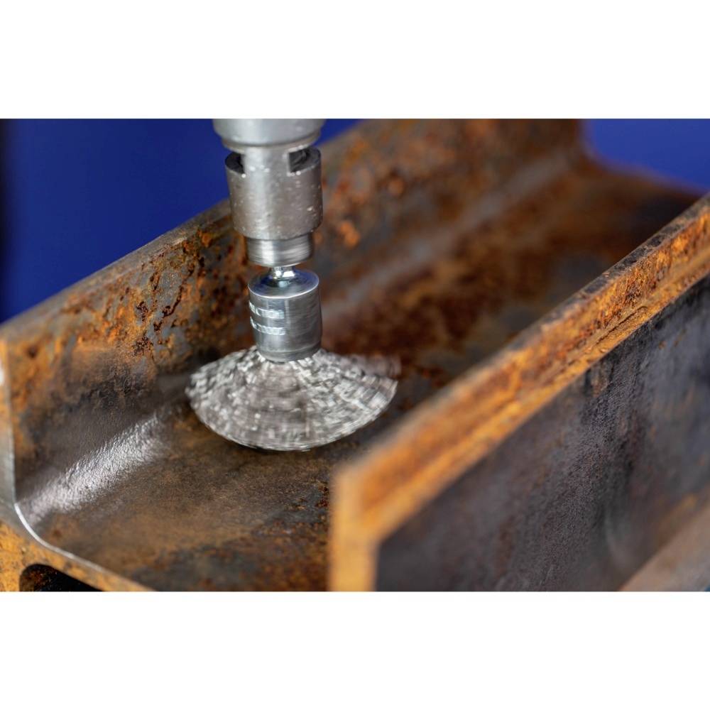 Ein rotierendes Drahtbürstenwerkzeug poliert eine verrostete Metalloberfläche. Der Prozess entfernt Rost und glättet das Metall.