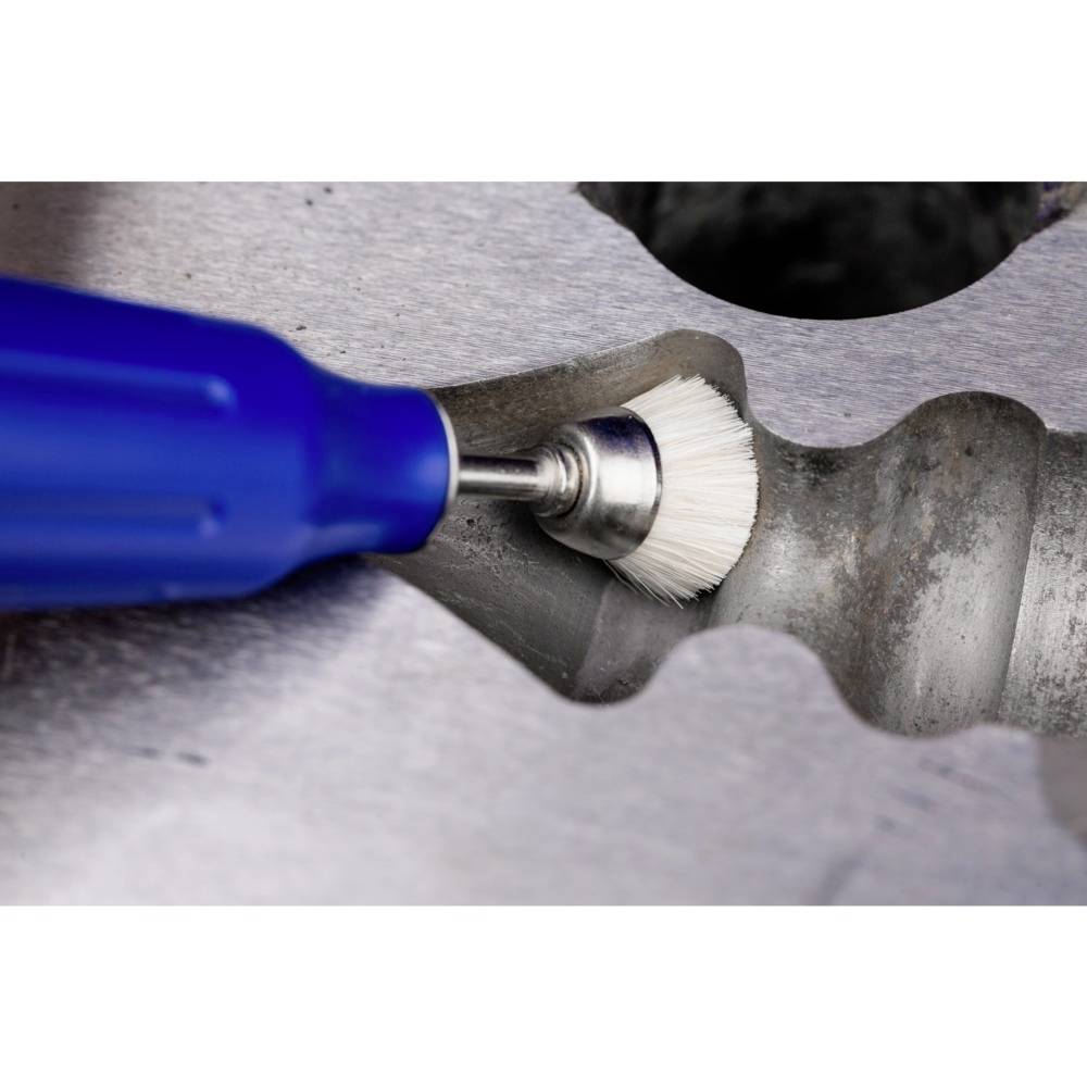 Ein blauer Pinsel reinigt eine Metalloberfläche mit einer Zahnrille. Der Fokus liegt auf der Reinigungsaktion im industriellen Kontext.