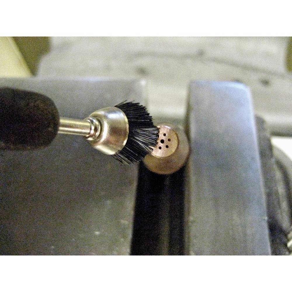 Bohrer mit Bürstenaufsatz reinigt ein Metallstück mit kleinen Löchern, das in einem Schraubstock eingespannt ist.