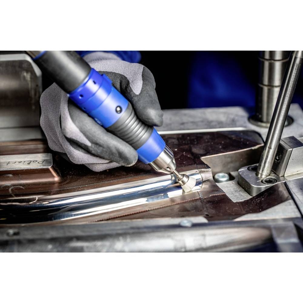 Eine Person bearbeitet ein Metallteil mit einem blauen, handgehaltenen Elektrowerkzeug. Handschuhe bieten Schutz.