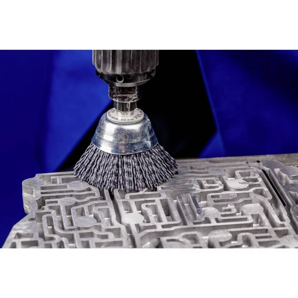 Eine elektrische Drahtbürste reinigt eine große Metallform auf einem Tisch, umgeben von einer Person in blauer Schutzkleidung.