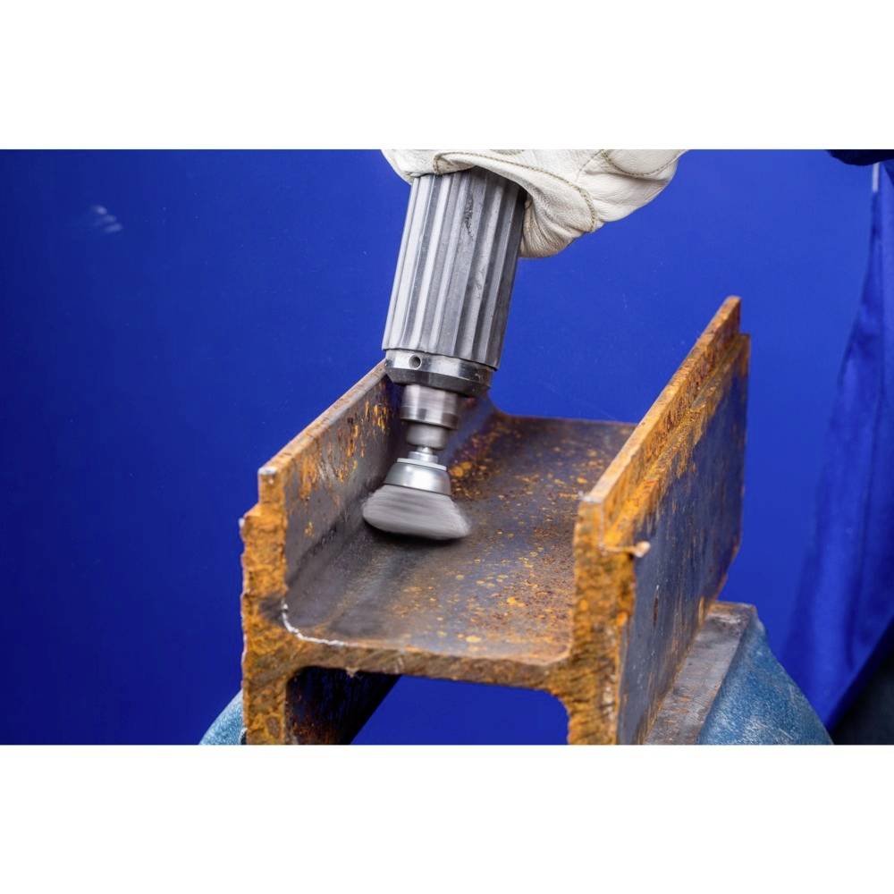 Eine Hand hält ein rotierendes Metallwerkzeug, das Rost von einem Stahlträger entfernt. Hintergrund blau.