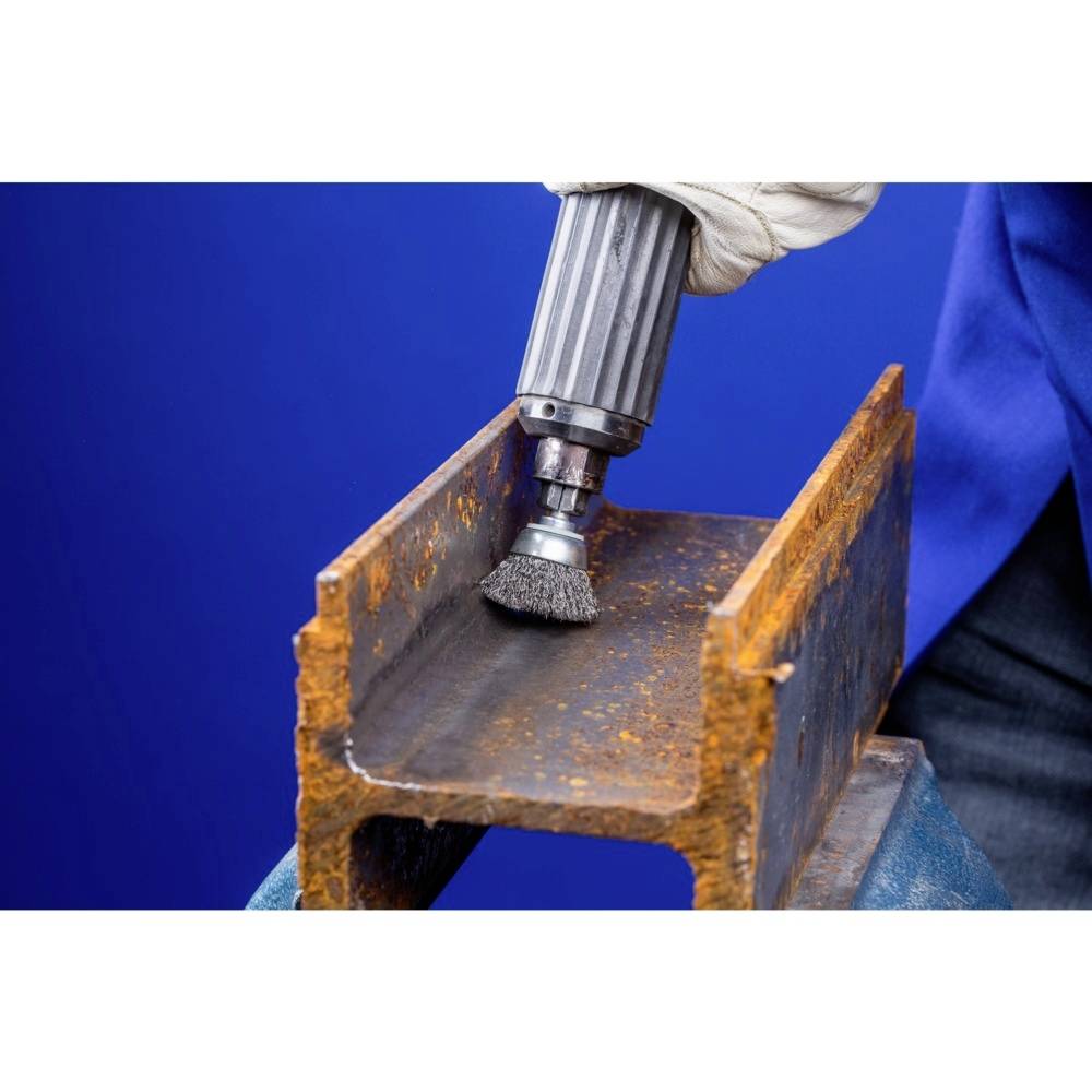 Ein Metallstück wird mit einer rotierenden Drahtbürste bearbeitet; die Oberfläche wird von Rost befreit. Hintergrund in Blau.