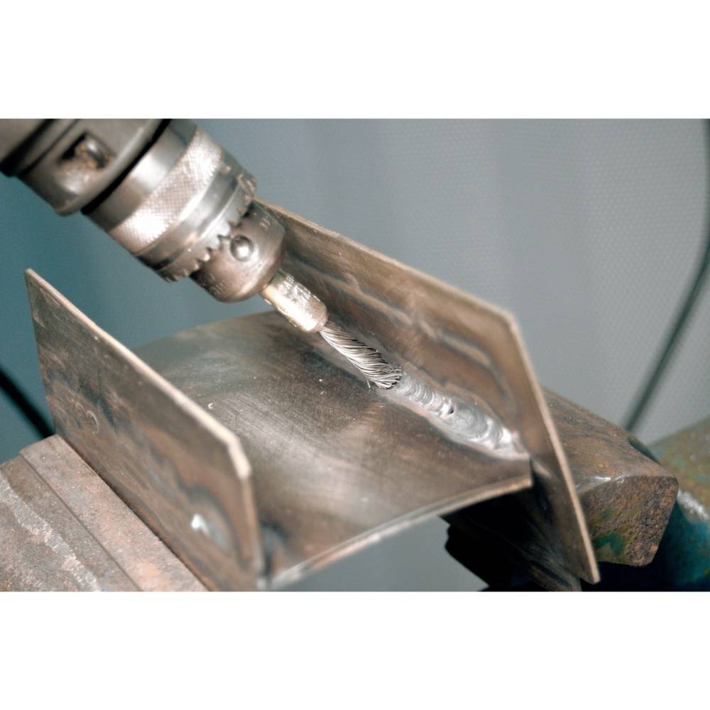 Eine Nahaufnahme zeigt einen Metallbohrer, der ein gebogenes Metallstück in einem Schraubstock bearbeitet.