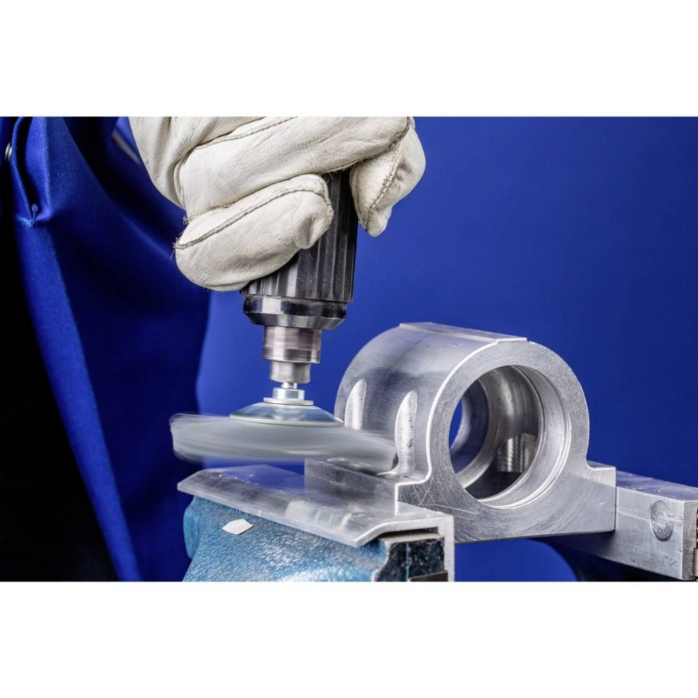 Ein Handwerker schleift eine Metalloberfläche mit einem elektrischen Schleifwerkzeug. Er trägt einen Schutzhandschuh.