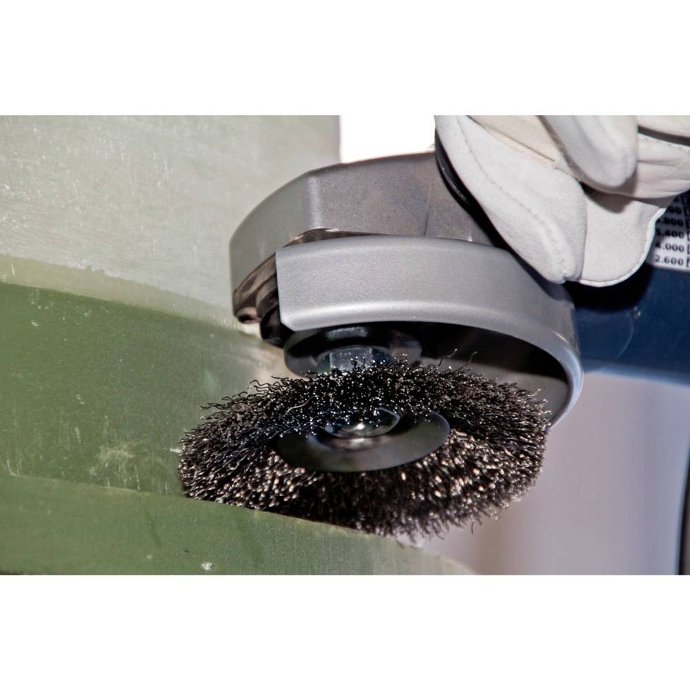 Eine Nahaufnahme einer Drahtbürste in Aktion, die mit einer Maschine Metall reinigt. Eine behandschuhte Hand hält die Maschine fest.