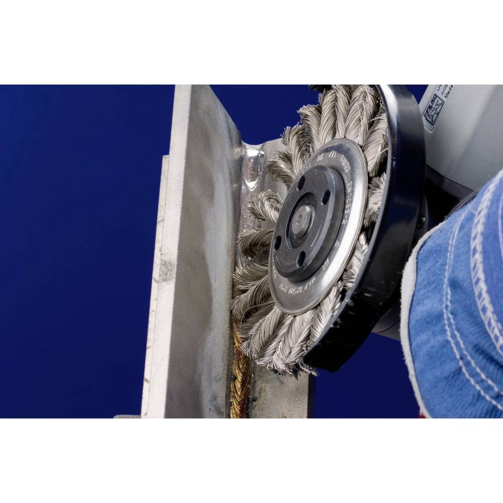 Eine Drahtbürste wird verwendet, um Rost von einer Metalloberfläche zu entfernen. Die Maschine ist teilweise sichtbar.