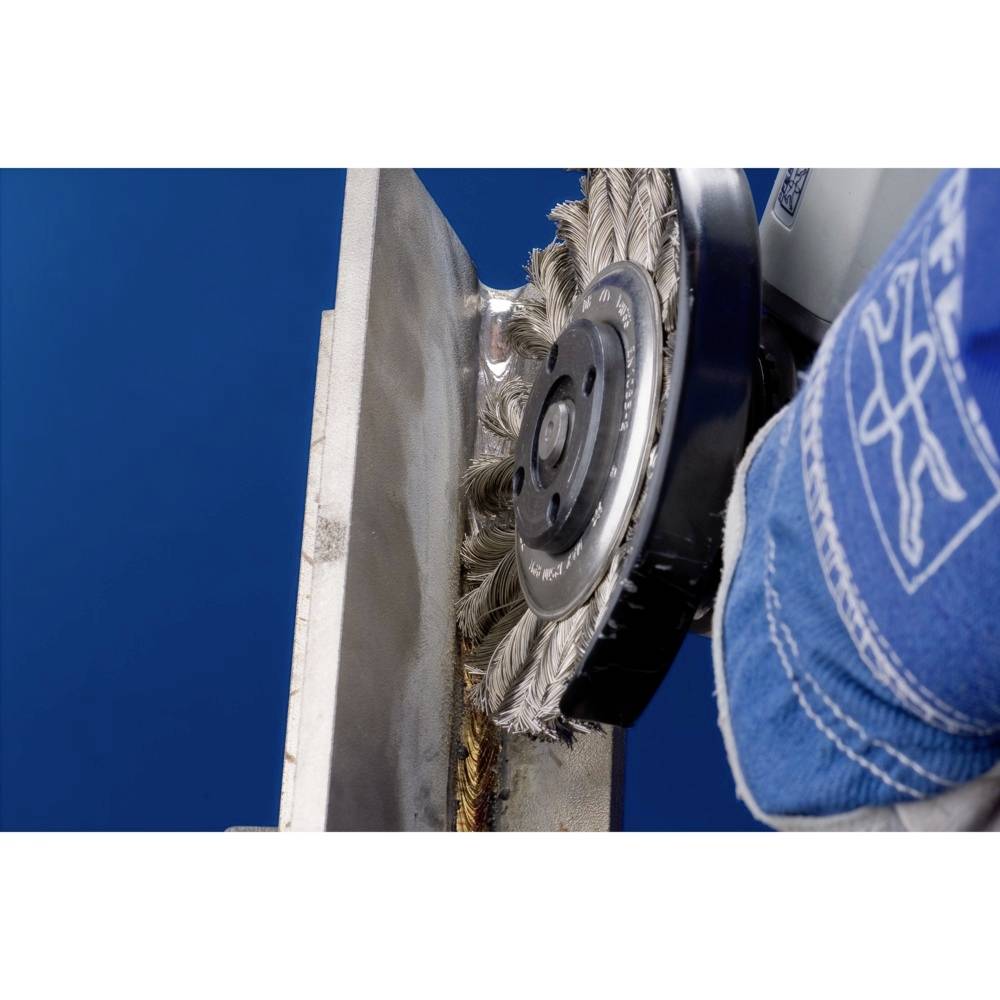 Eine Drahtbürste reinigt die Kante einer Metallplatte. Ein blauer Hintergrund ist zu sehen. Arbeiter trägt blaue Schutzkleidung.