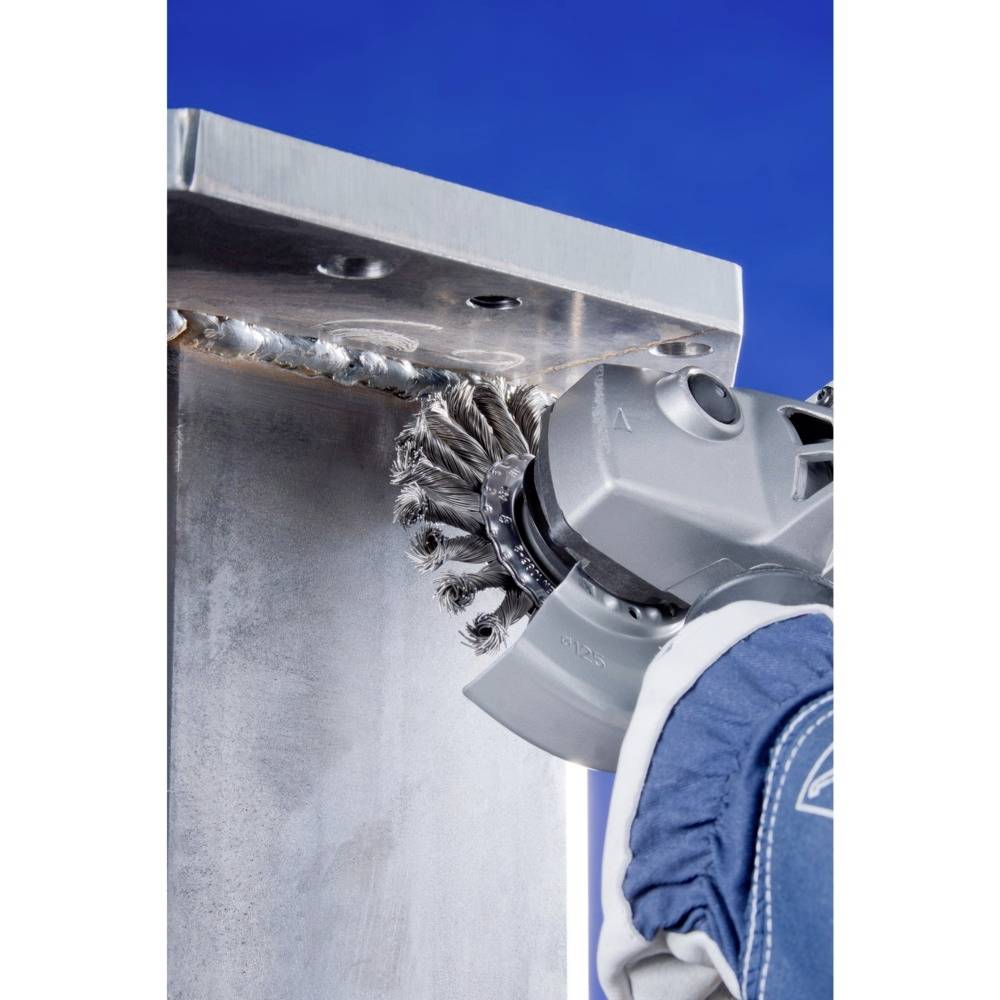 Ein Handwerker verwendet ein Schleifwerkzeug, um Schweißnähte auf einem Metallträger zu glätten. Der Himmel ist blau im Hintergrund.