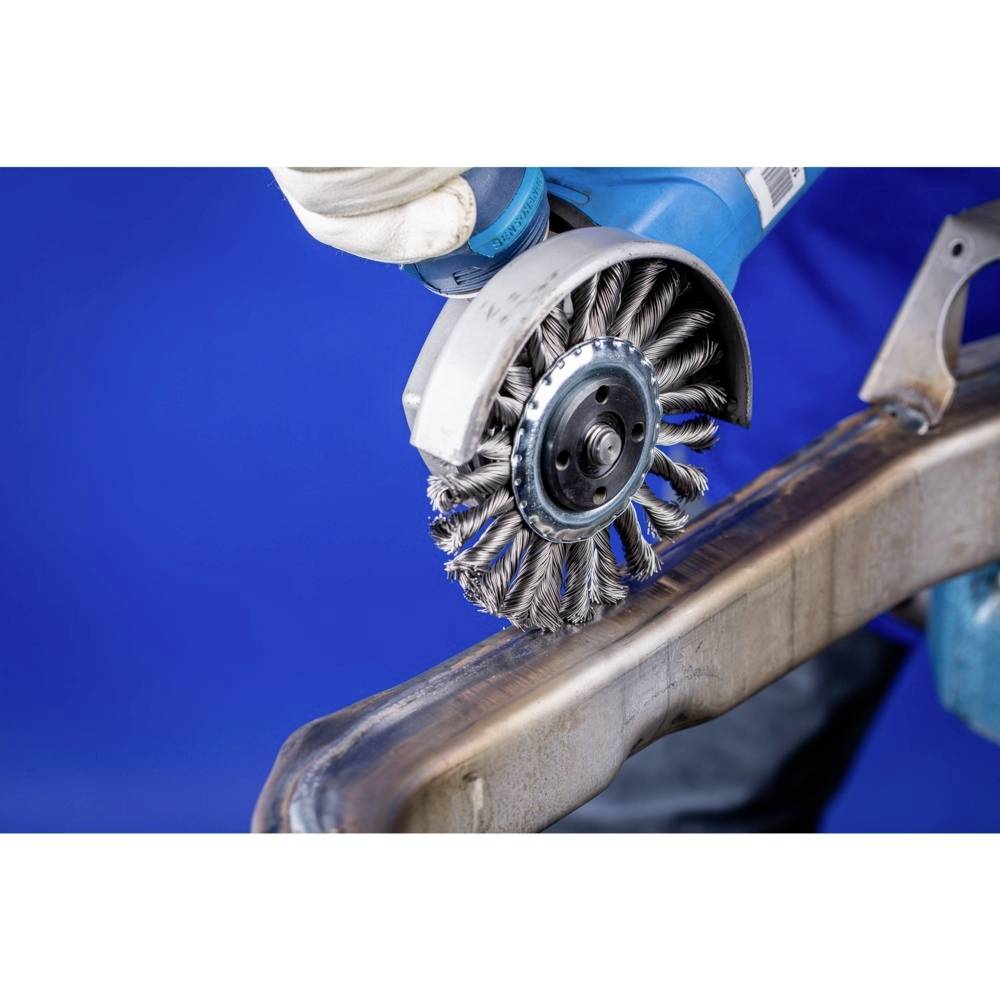 Eine Person verwendet eine elektrische Drahtbürste zur Metallbearbeitung auf einer Metallfläche vor blauem Hintergrund.