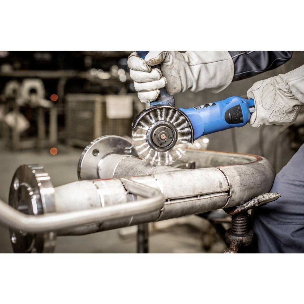 Handwerksperson schneidet Metallrohr mit Winkelschleifer. Schutzhandschuhe getragen. Funken fliegen. Werkstatt im Hintergrund.