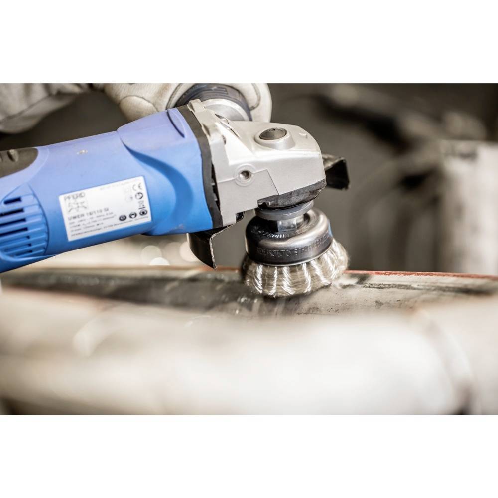 Eine Hand hält einen Winkelschleifer, der eine Metalloberfläche poliert. Fokus auf die rotierende Drahtbürste des Werkzeugs.