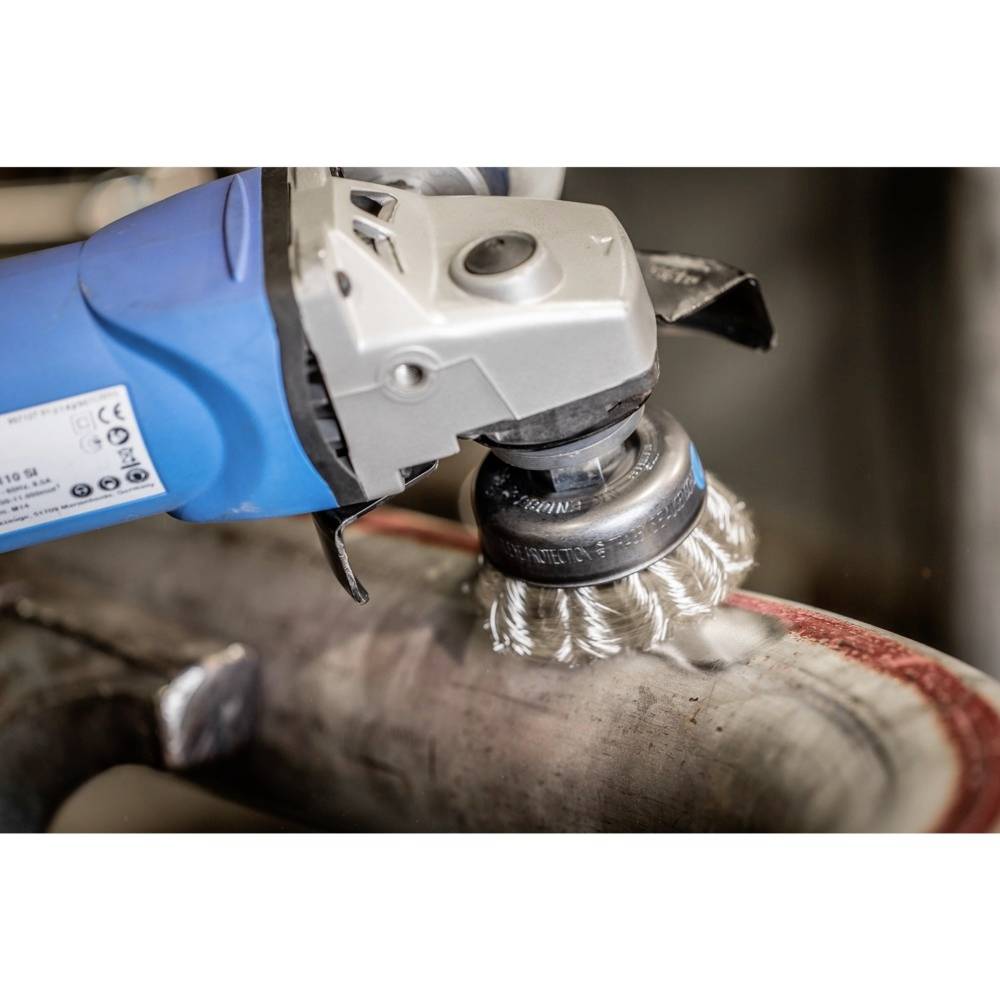 Eine elektrische Schleifmaschine bearbeitet eine Metalloberfläche. Die Maschine hat einen blauen Griff und eine runde Bürste zur Politur.