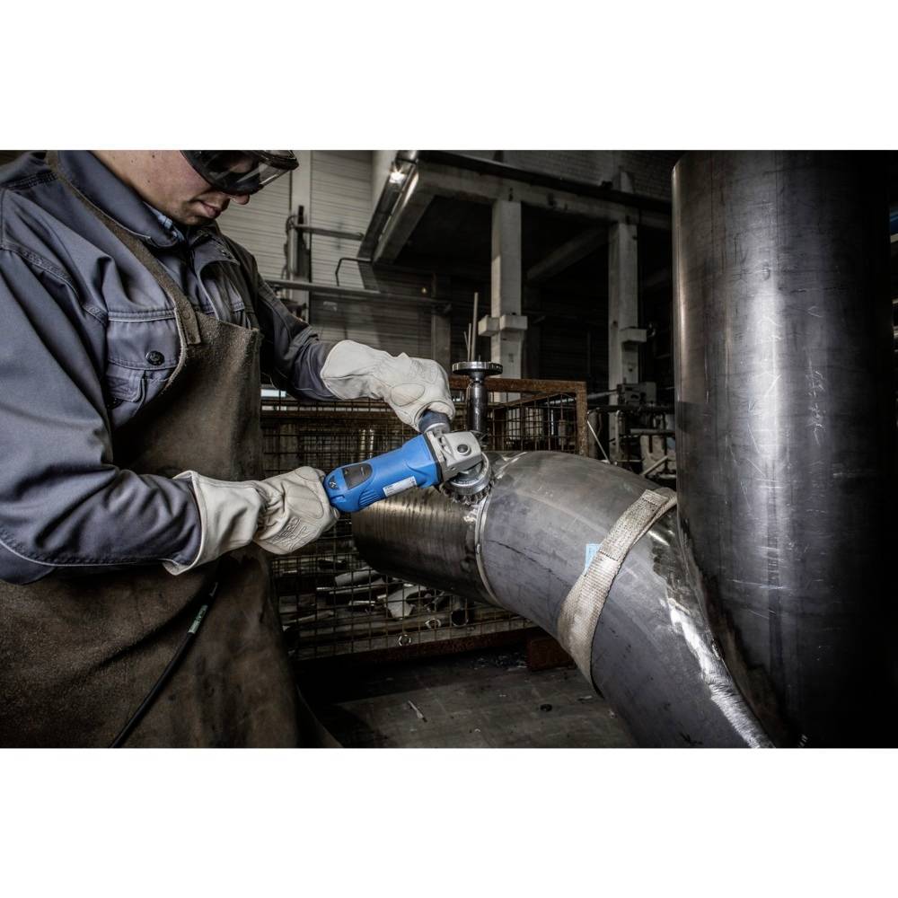 Eine Person schleift ein gekrümmtes Metallrohr mit einem blauen Winkelschleifer in einer industriellen Werkstatt, trägt Schutzkleidung.