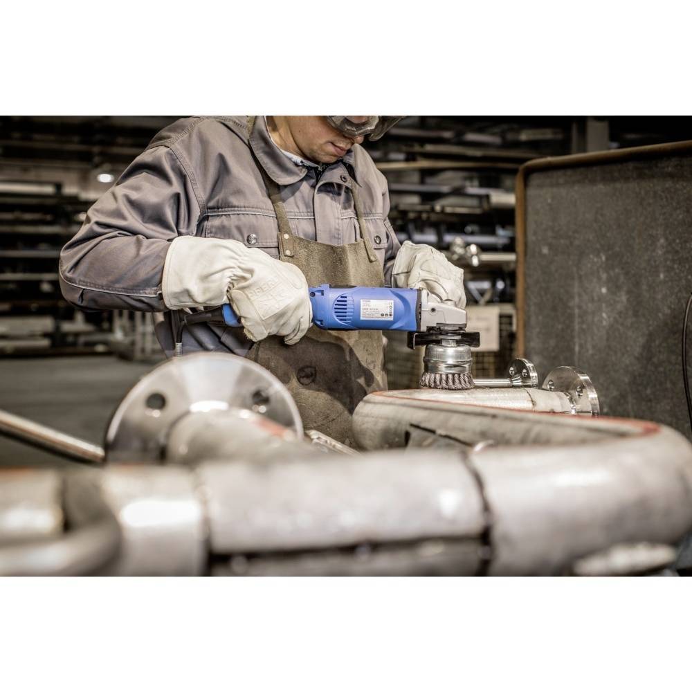 Eine Person in Arbeitskleidung und Schutzbrille schleift ein Metallrohr in einer Werkstatt. Sie verwendet ein elektrisches Schleifwerkzeug.