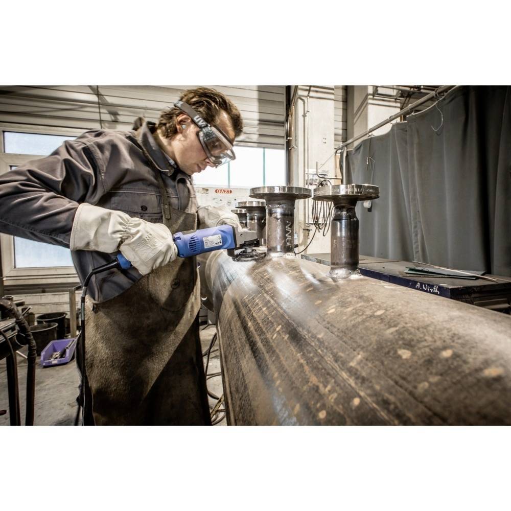 Ein Arbeiter mit Schutzbrille und Handschuhen schweißt oder bearbeitet Metallrohre in einer Werkstattumgebung.