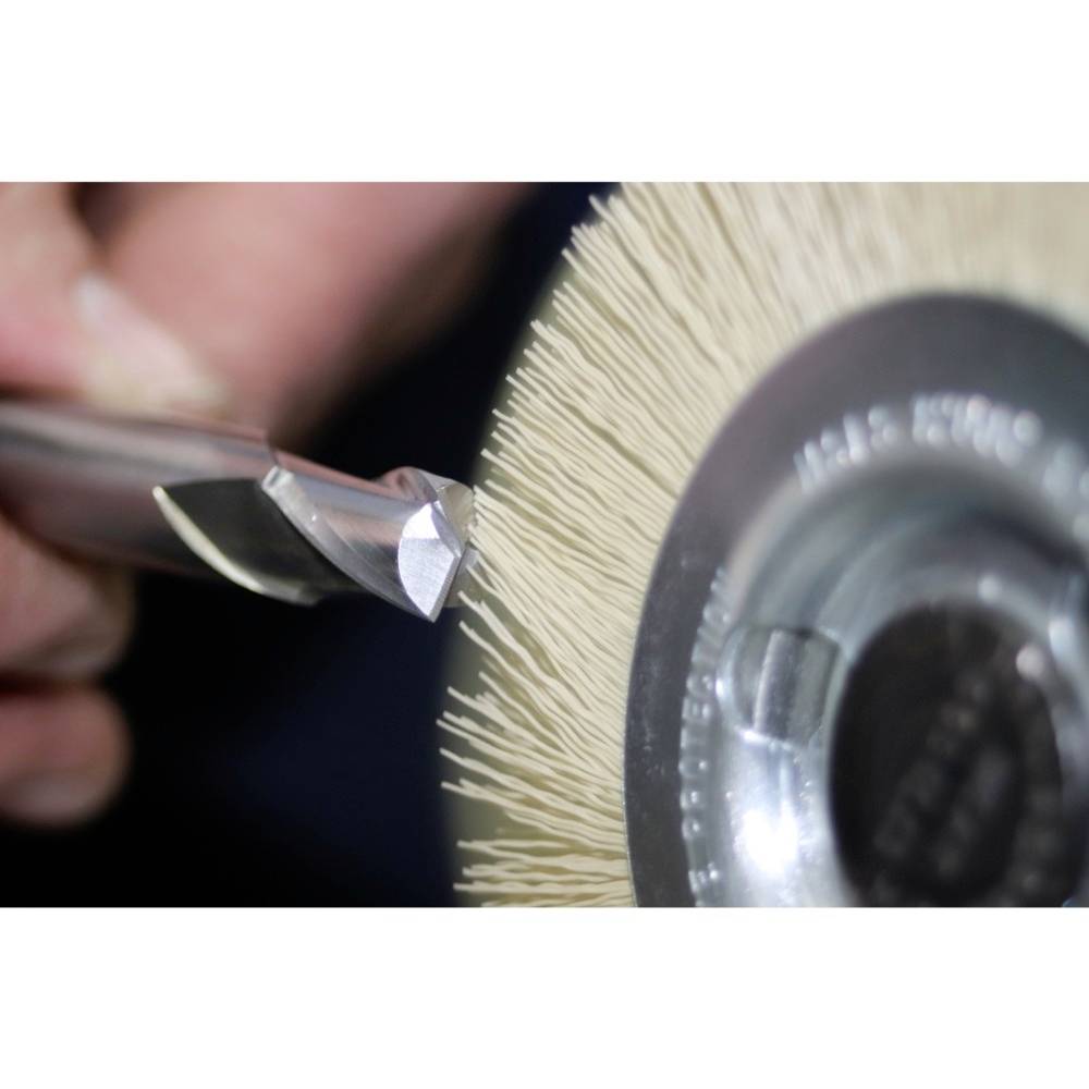 Nahaufnahme eines rotierenden Schleifrads, das eine Metallklinge schärft. Hände halten das Werkzeug präzise an die Schleifstelle.